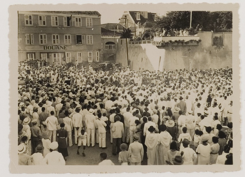 Toeschouwers op de hoek van de Breedestraat en het Gouvernementsplein in Willemstad bij de historische optocht ter gelegenheid van de driehonderdjarige herdenking van de verovering van Curaçao