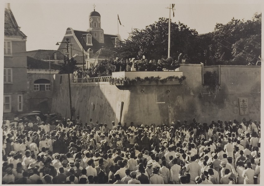 Gouverneur G.J.J. Wouters (op het bordes) en toeschouwers op de hoek van de Breedestraat en het Gouvernementsplein bij een optocht in Willemstad op Curaçao