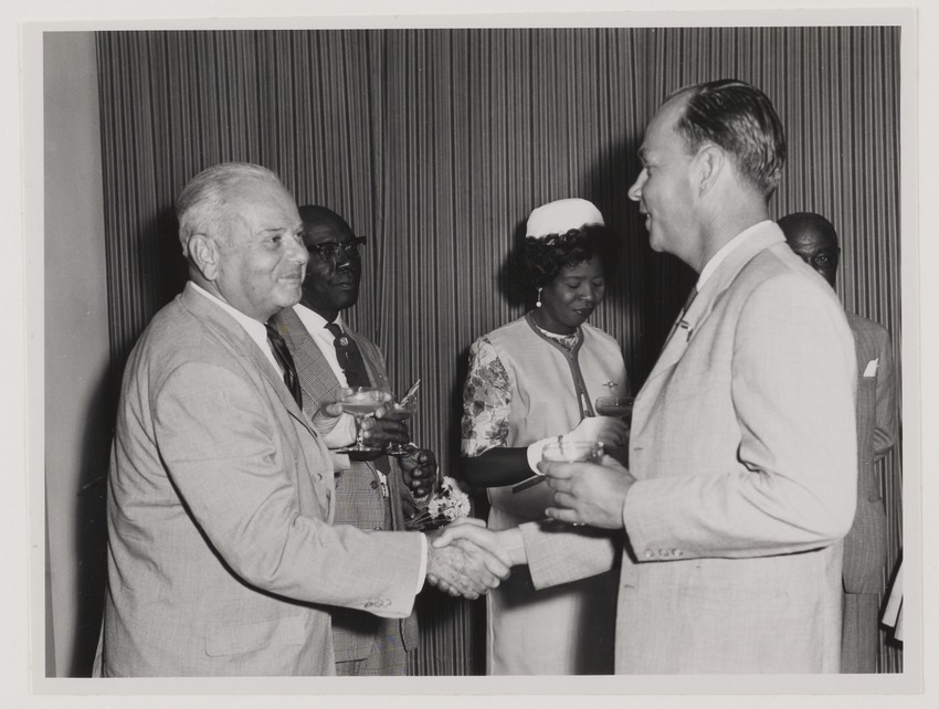 J.C. van Essen (links), hoofd Fotografische Dienst van de N.V. Shell Curaçao, wordt gefeliciteerd door (vermoedelijk) Ron Storm bij zijn benoeming tot Ridder in de Orde van Oranje Nassau in het gouverneurshuis te Willemstad