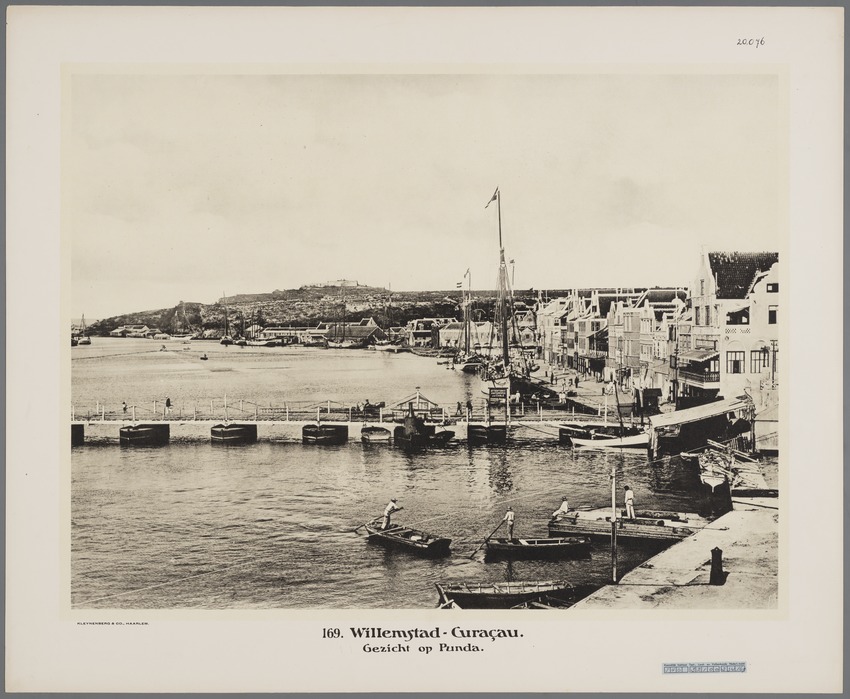 Twee schoeners (rechts) achter de Koningin Emmabrug aan de kade van de wijk Punda in Willemstad op Curaçao met in het eerste gebouw rechts, het zogenaamde Penhagebouw, Club De Gezelligheid en op de achtergrond Fort Nassau