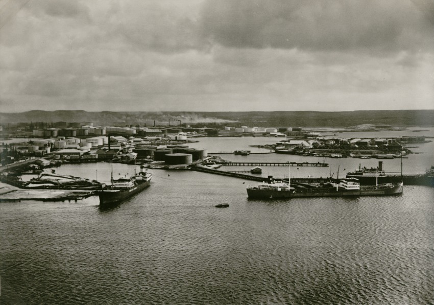 Op de voorgrond een deel van Emmastad op Curaçao en op de Tankers bij de raffinaderij te Emmastad van de Curaçaosche Petroleum Industrie Maatschappij